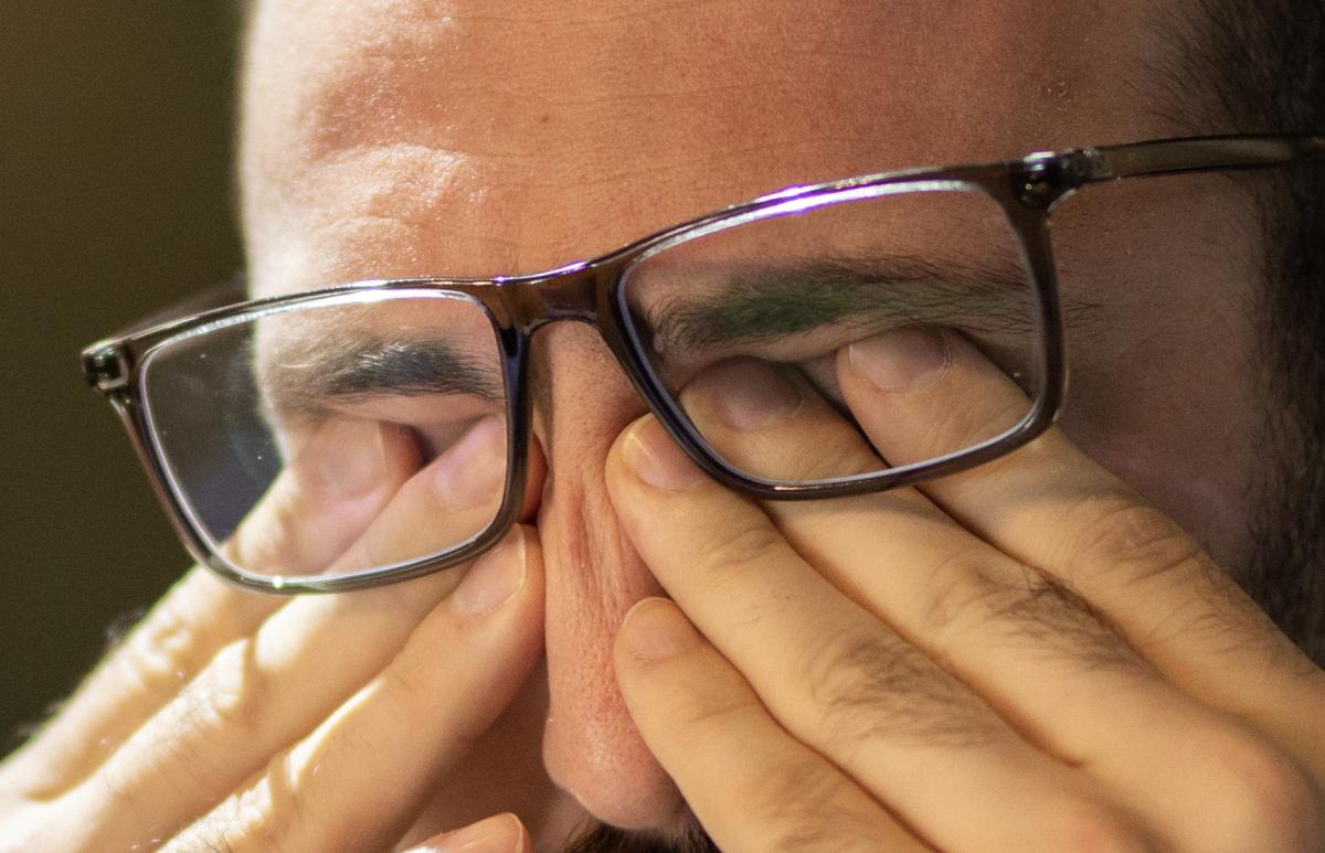 Man with glasses rubs eyes in gesture of fatigue.