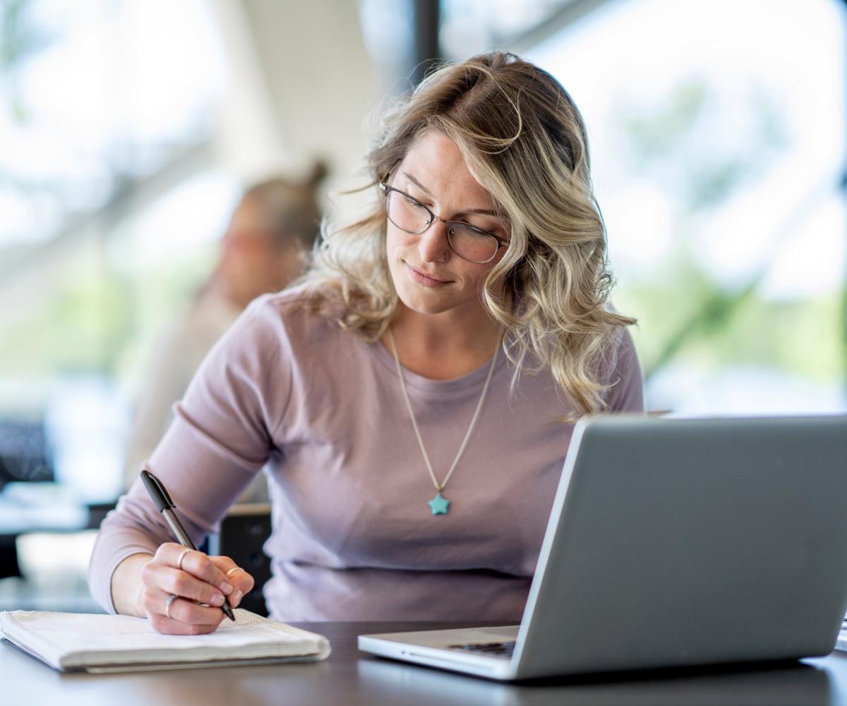 Female student with laptop taking notes.